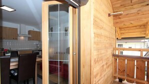 Un interior de madera con cocina, una mesa de comedor con sillas y un balcón con barandilla de madera.