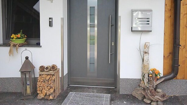 Una puerta moderna con el número 4 encima, una pequeña ventana y una maceta, además de un cuadro de empalmes eléctricos en la pared.