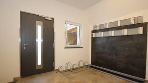 Una habitación con una puerta oscura, una ventana, una estantería metálica y un panel grande y oscuro en la pared.