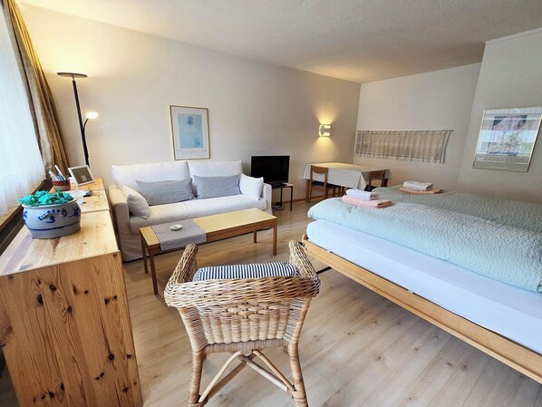 Een gezellige hotelkamer met een bed, bank, eettafel en een rieten stoel.