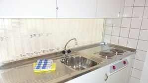 Una cucina con lavello in acciaio inossidabile, due piastre cottura e un forno a microonde.