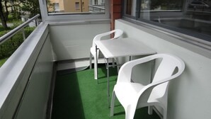 Un balcone con un tavolino e due sedie, un pavimento in erba sintetica verde e una finestra vista edifici.