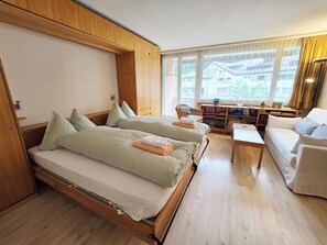 Een kamer met twee bedden, een bank, een kleine tafel en een raam met uitzicht op gebouwen.