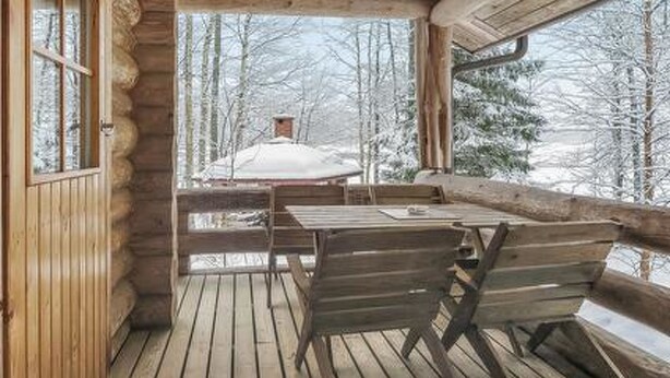 A wooden deck with a table and chairs, overlooking a snowy forest.