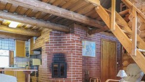A cozy log cabin interior with a brick fireplace, wooden beams, and a dining area.