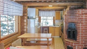 A cozy cabin-style kitchen with a brick fireplace, wooden furniture, and large windows.