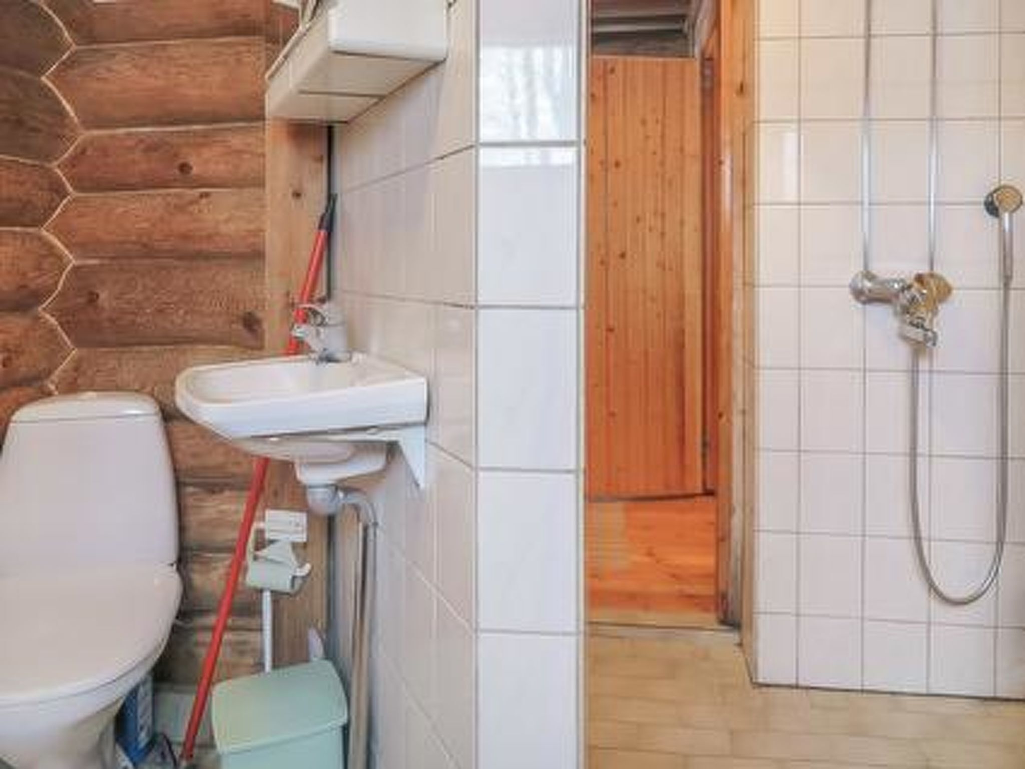 A bathroom with a wooden wall, a white sink, a toilet, and a shower.