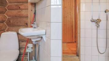A bathroom with a wooden wall, a white sink, a toilet, and a shower.