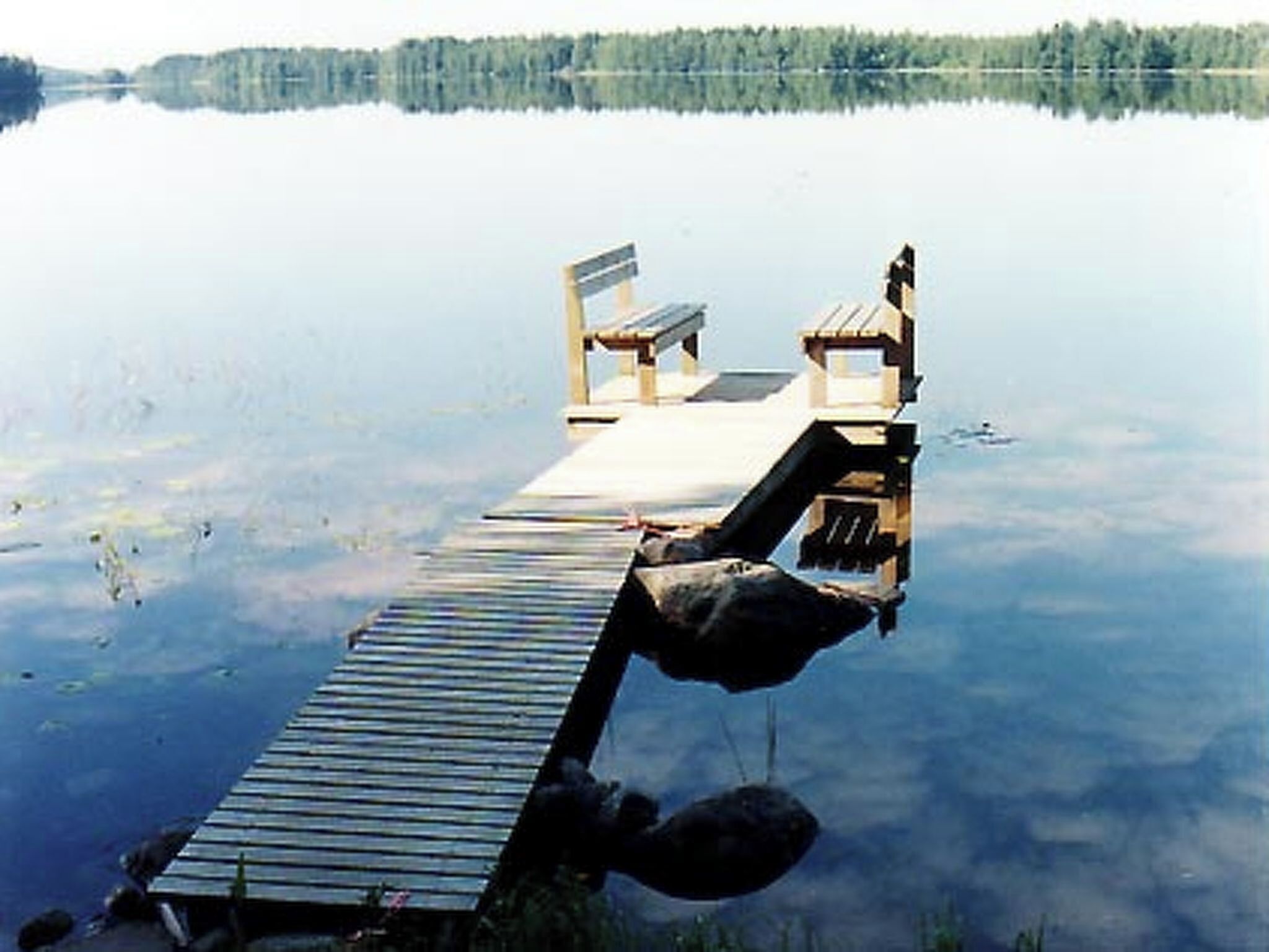 A wooden dock extending into a calm lake with a bench at the end.