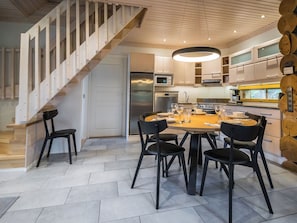 A modern kitchen with a dining area, featuring a wooden staircase, contemporary appliances, and a round table with chairs.