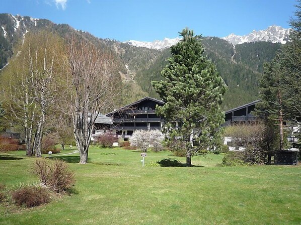 A lodge with multiple rooms, surrounded by a well-maintained lawn and trees, with a mountain backdrop.