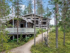 A log cabin with a deck, surrounded by trees and a gravel path. - Villa mitja by Interhome (Posio)