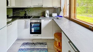 Eine moderne Küche mit weißen Schränken, einem eingebauten Backofen, einer Kaffeemaschine und einem Fenster mit Blick auf Grünflächen.