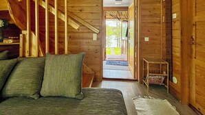 Ein Holzblock-Innenraum mit Bett, kleinem Tisch und einer Tür zu einem Außenbereich.