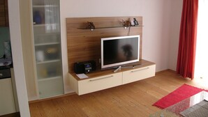 Ein modernes Wohnzimmer mit einem Flachbildfernseher auf einer Holzkommode, einer Glasscheibe und einem roten Vorhang.