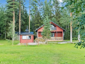 A red cabin with a balcony, surrounded by a grassy area and trees.
