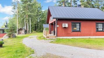 Een rode houten chalet met een metalen dak, een grindpad naar de ingang en een bebost achtergrond.