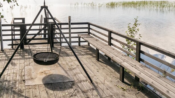 Une jetée en bois avec une rambarde en métal, un banc et un gril en métal.