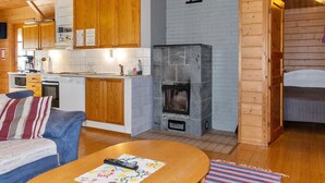 L’intérieur chaleureux d’un chalet avec des murs en bois, un coin cuisine doté de meubles en bois, une cheminée en pierre et un salon comprenant un canapé et une table basse.