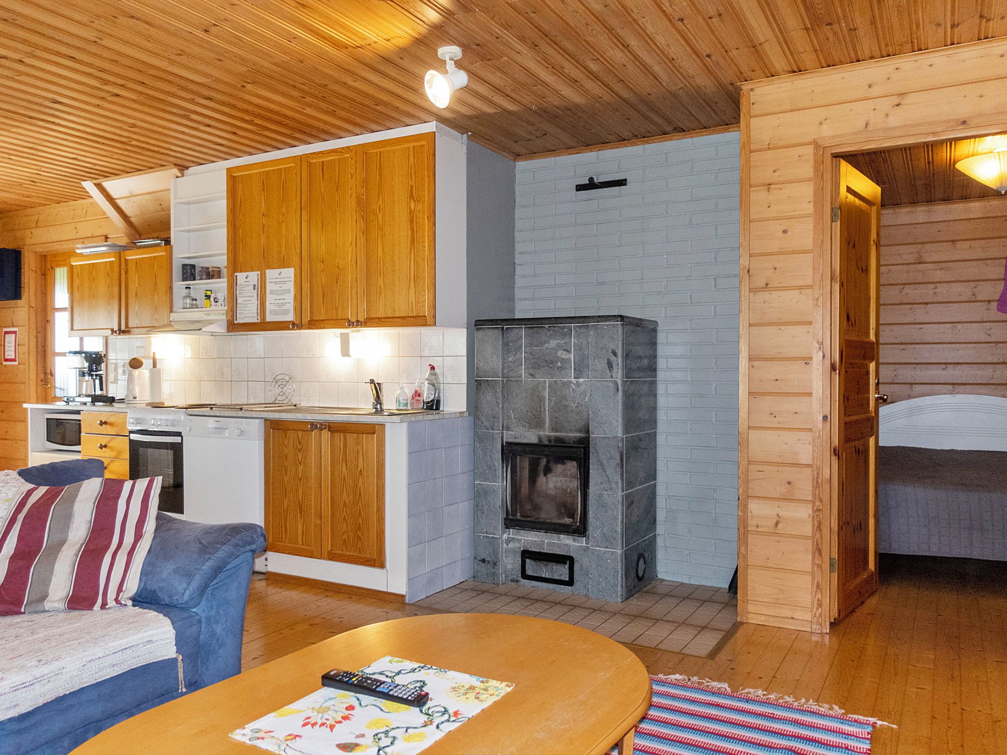Interior acogedor de una cabaña con paredes de madera, una zona de cocina, una chimenea y un espacio de estar con un sofá y una mesa de centro.