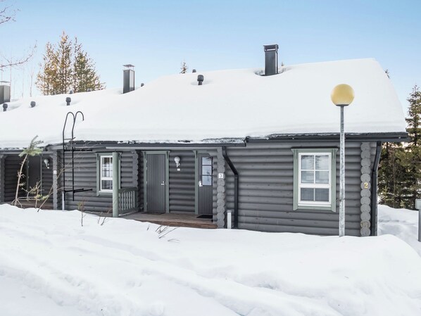 A log cabin with a snow-covered roof, a front porch, and a chimney.