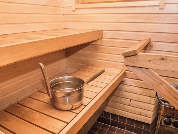 A sauna room with a wooden bench, a metal basin, and a sauna heater.
