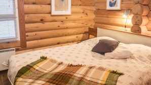 Ein gemütliches Blockhaus-Zimmer mit einem Bett, einer Karo-Decke und zwei gerahmten Kunstwerken an der Wand.