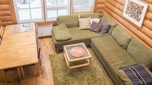 Ein gemütliches Blockhauss-Interieur mit einem grünen Sofa, einem kleinen Holztisch und einem Fenster mit Jalousien.
