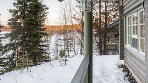 Eine Holzhütte mit verschneitem Deck und Blick auf eine bewaldete Landschaft.