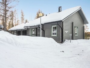 A log cabin with a snow-covered roof, a chimney, and a small porch area.