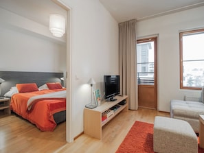 A modern hotel room with a bed, a TV, a desk, and a window with curtains.