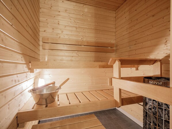 A sauna room with wooden walls, a bench, a bucket, and a metal container labeled 'HARVIA'.