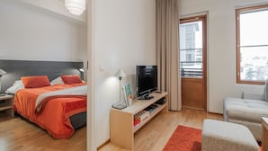 Une chambre d’hôtel moderne équipée d’un lit, d’une télévision, d’un bureau et d’une fenêtre donnant sur des immeubles.