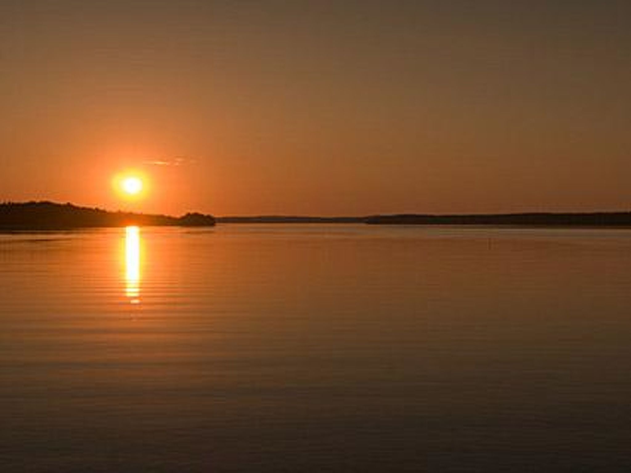 A sunset over a calm body of water with a distant shoreline.