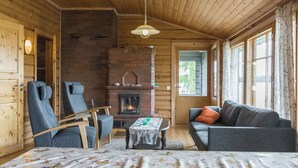 A log cabin interior with a fireplace, wooden walls, a sofa, a chair, and a table. - Katajainen by Interhome (Ikaalinen)