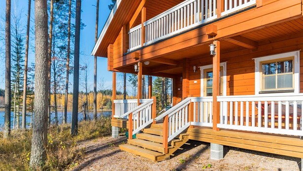 Een houten chalet met een balkon, een veranda en uitzicht op een meer, omringd door bomen.