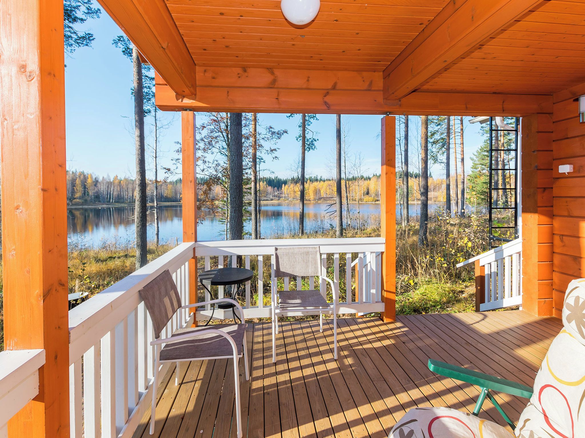 Une terrasse en bois avec une table et des chaises, donnant sur un lac entouré d’arbres.