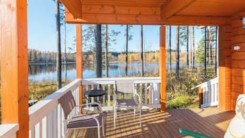 A wooden deck with a table and chairs, overlooking a lake surrounded by trees.
