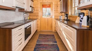 Een smalle keuken met houten wanden en kastjes, een centrale deur en een kleurrijk vloerkleed.
