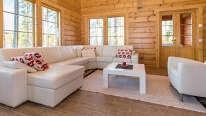 Een interieur van een blokhut met een witte modulaire bank, een salontafel en een witte fauteuil.