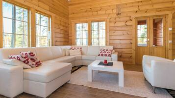 A modern log cabin interior with a sectional sofa, a coffee table, and a white armchair.
