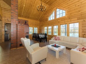 A spacious wooden interior with a dining area, a fireplace, and a large window offering a view of the outdoors.
