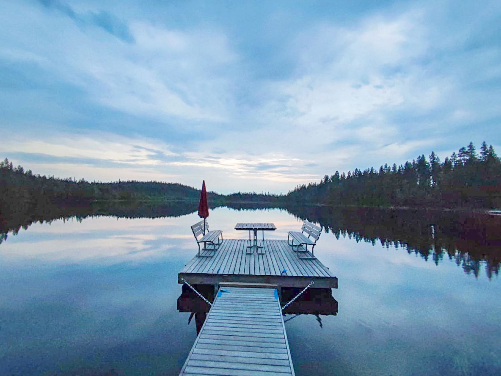 A wooden dock extending into a calm lake with a table and benches, surrounded by forested hills.