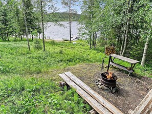 Uma área de camping com lareira, um banco e vista para um lago.