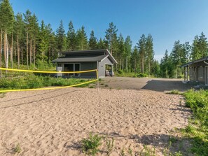 Una cancha de voleibol de playa con una red, un pequeño edificio y un bosque al fondo.