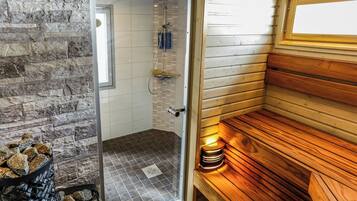 Un sauna avec une porte en verre donnant sur un espace douche, des bancs en bois et un mur en pierre.