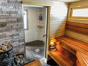 Un sauna avec une porte en verre donnant sur un espace douche, des bancs en bois et un mur en pierre.