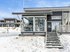 Une maison moderne à deux étages, dotée de grandes fenêtres, d’un porche abrité et d’une allée recouverte de neige.