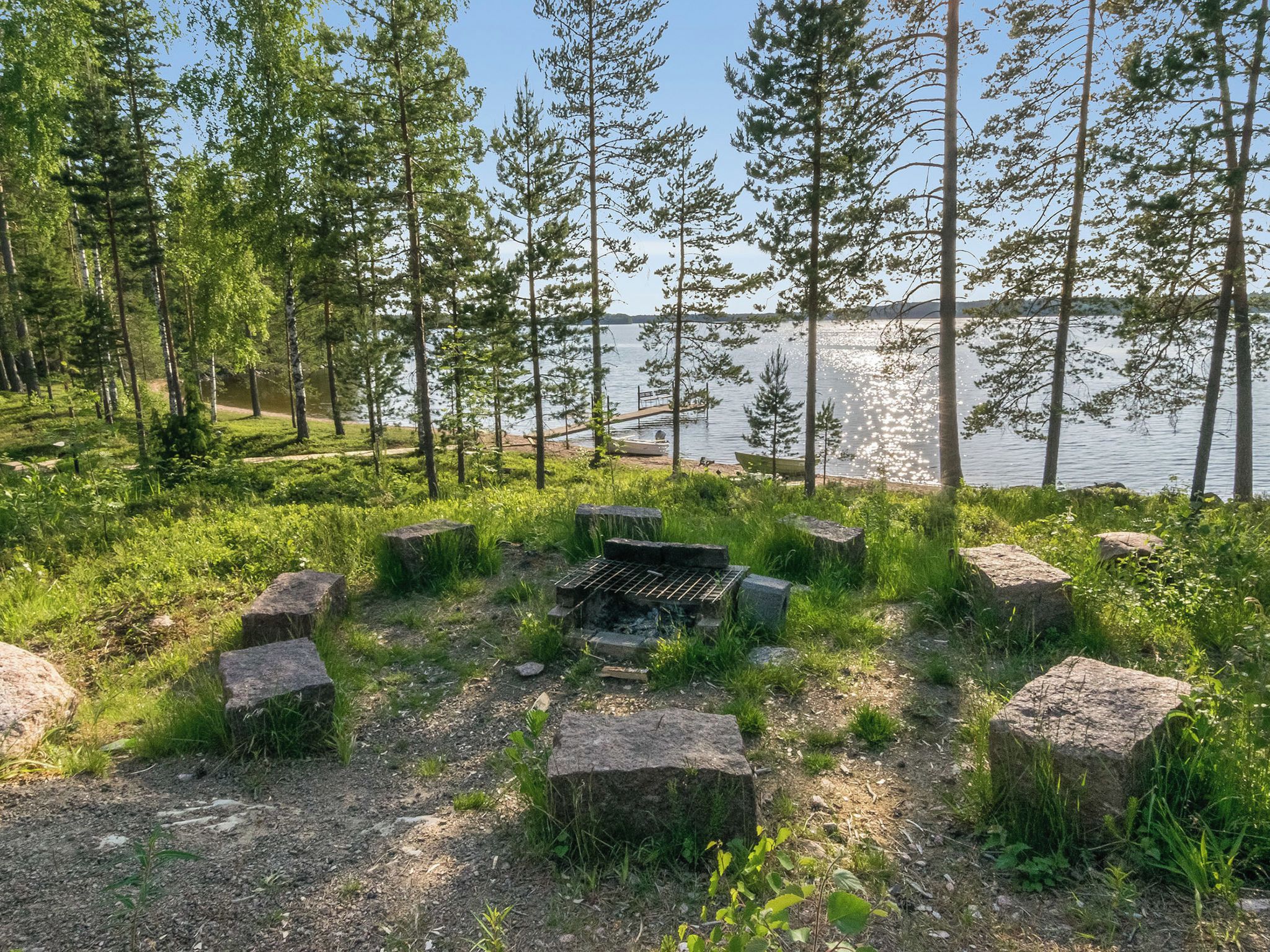 Un camping con un pozo de fuego rodeado de rocas, un lago y árboles al fondo.
