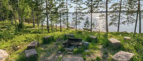 Een camping met een vuurkuil, omringd door rotsen, een meer en bomen op de achtergrond.